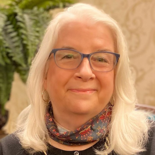 headshot of a woman with medium length white hair, glasses, and a patterned scarf